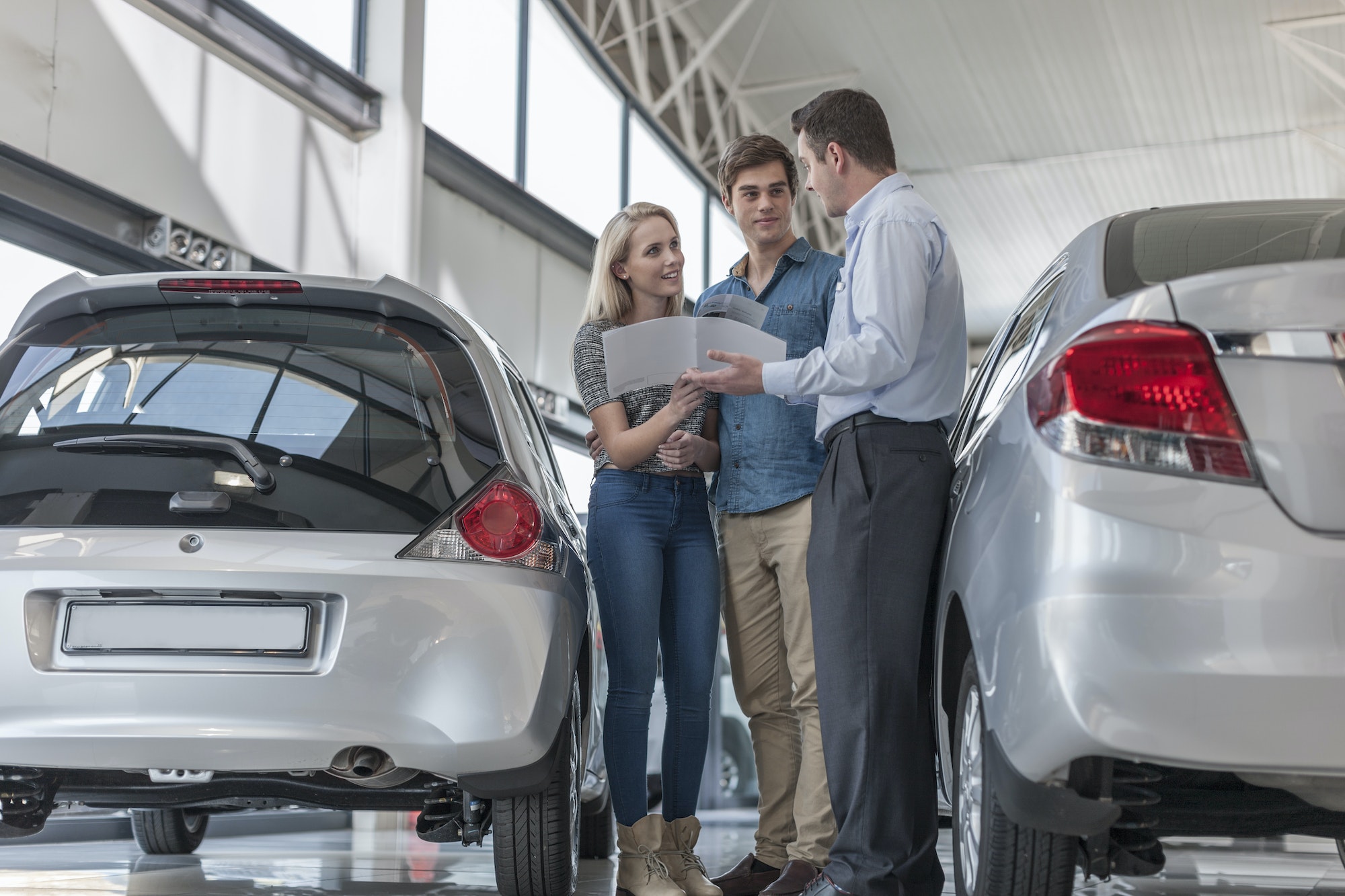 Car dealer showing brochure to young couple in showroom